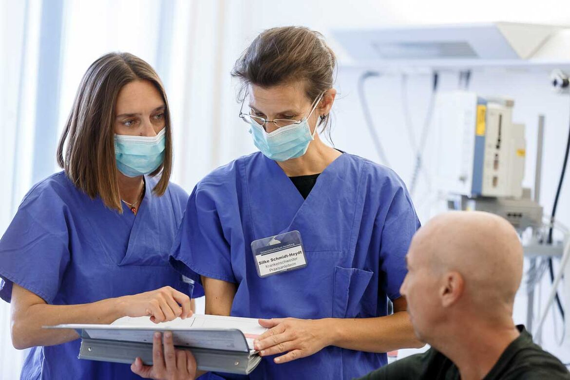 Zwei Mitarbeitende der Station von Dusch im Patientengespräch am Krankenhausbett.